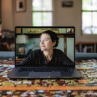 A woman is pictured on the screen of a laptop computer sitting on a table filled with puzzle pieces