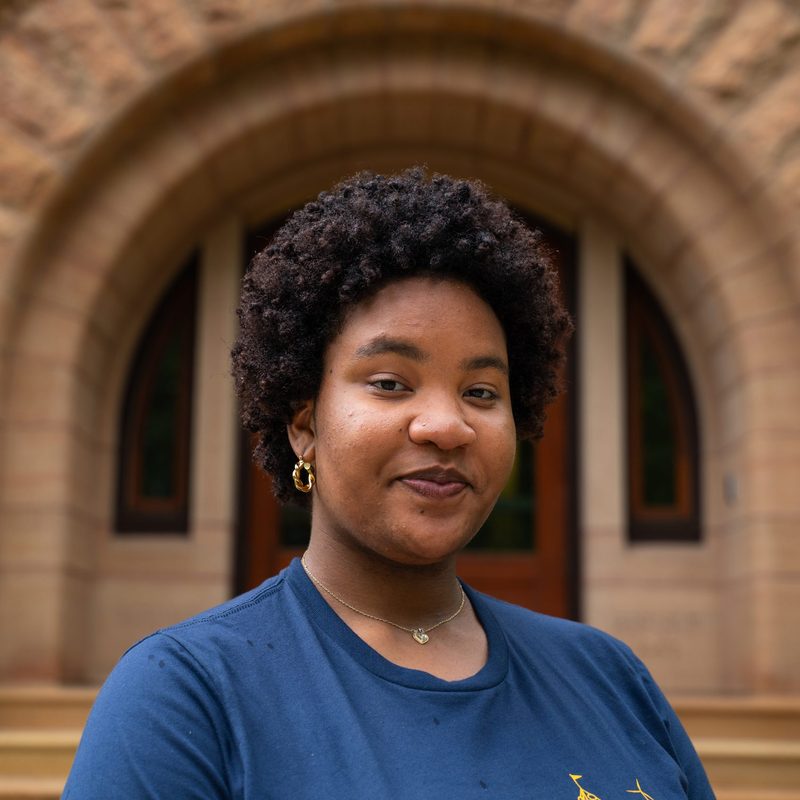 Yahnee Acklin '25 stands in front of the admissions building and looks into the camera.