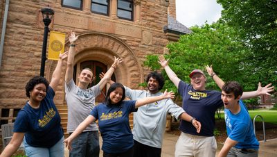 6 students celebrating with their hands up in front of Scoville Hall