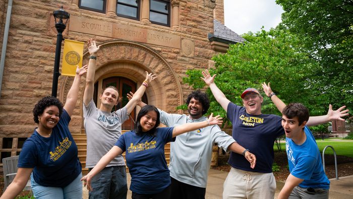 6 students celebrating with their hands up in front of Scoville Hall