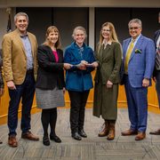 Carleton and St. Olaf administrators hand checks to the Northfield mayor as they pose and smile for the camera.
