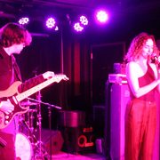 Rebecca McCartney singing into microphone accompanied on stage by bass guitarist