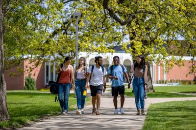 students walk through a tree shaded part of campus in the summer