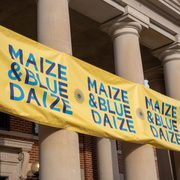 Close-up on the Maize & Blue Daize banner attached to the columns of Sayles-Hill Campus Center.
