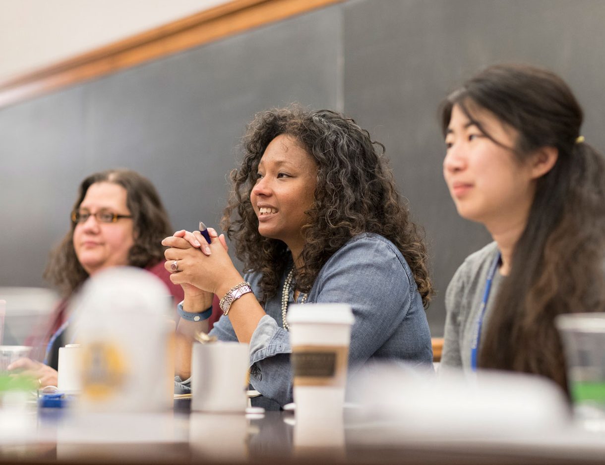 Three women sit at a table in front of a blackboard