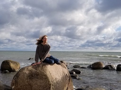 A student sits on a rock on an ocean beach