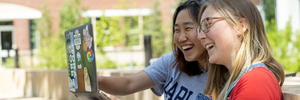 two students sharing laptop outside smiling