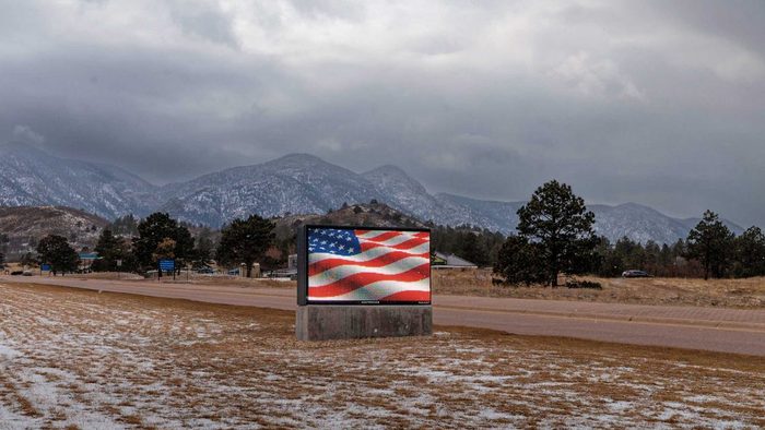a digital american flag on a tv-billboard surrounded by snow, grass, and mountains.