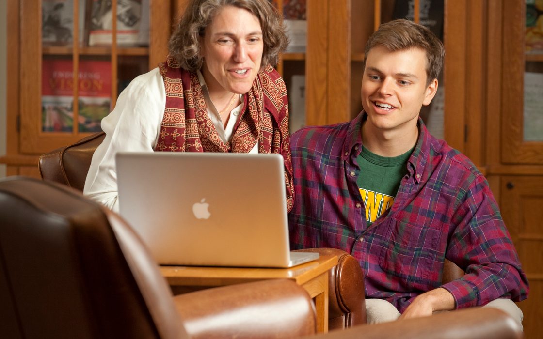 Professor and student look at an open laptop