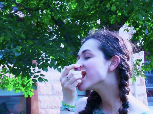 A young woman stands under a tree eating an apple