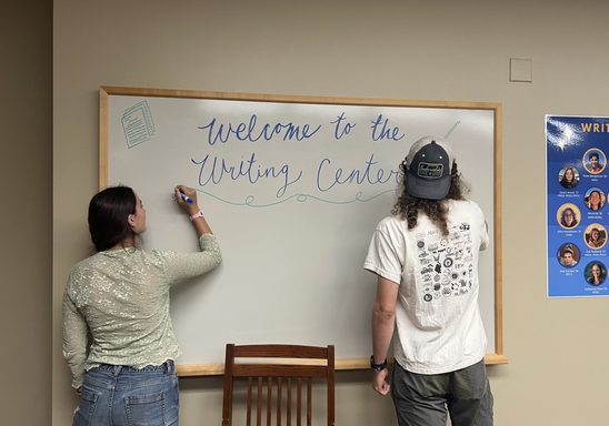 Two students draw on the Writing Center's white board