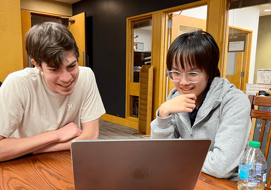 Two students leaning over a laptop in the Writing Center